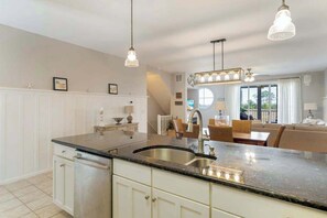 Cuina moderna amb una illa gran, il·luminació penjant i vista a una zona d'estar.
