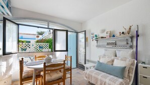 A room with a bed, a table with chairs, a window with a view of buildings, and a shelf with decorative items. - Studio on La Corniche with Shared Pool, Private Terrace, and Shared Garden (Saint-Palais-sur-Mer)