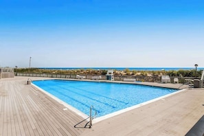 Et rektangulært swimmingpool med en træterrasse, omgivet af et hegn, og udsigt til havet.
