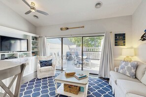 A living room with a television, a ceiling fan, a coffee table, a sofa, and a view through a sliding glass door to an outdoor patio. - Sea Colony West condo with lovely deck, pools, hot tubs, tennis, & beach shuttle (Bethany Beach)