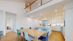 A spacious kitchen with white cabinets, a wooden dining table, and colorful chairs.