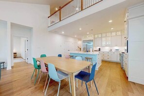 A spacious kitchen with white cabinets, a wooden dining table, and colorful chairs. - Bethany Beach Marlin Chase Ultra Luxe with pool, EV charging, pickleball & more (Ocean View)