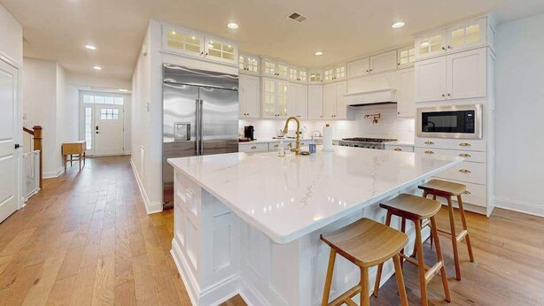 A spacious kitchen with white cabinetry, a large island, and wooden stools.
