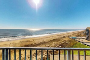 A beach view with a clear sky, a sandy shore, and a building with a balcony. - Sea Colony Oceanfront Penthouse - Views, Wrap-Around Deck, Pools, Private Beach (Bethany Beach)