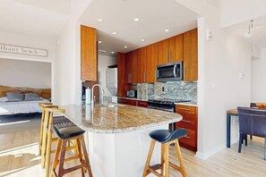 A modern kitchen with wooden cabinets, a granite countertop, and a central island with stools. - Sea Colony Oceanfront Penthouse - Views, Wrap-Around Deck, Pools, Private Beach (Bethany Beach)