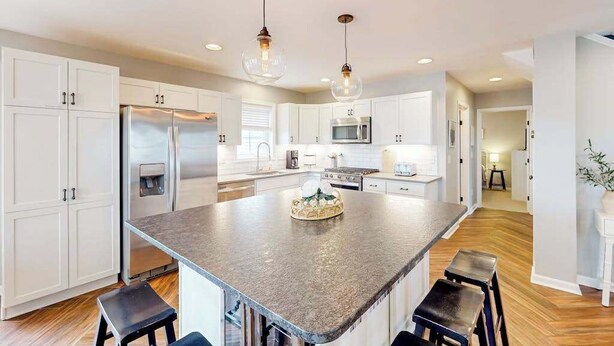 A spacious kitchen with white cabinets, a granite island, and pendant lighting. - Town of Bethany Beach designer cottage with water views, alfresco porch & AC (Bethany Beach)