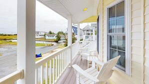 A porch with white railings and chairs, overlooking a residential area with houses and a body of water. - Town of Bethany Beach designer cottage with water views, alfresco porch & AC (Bethany Beach)