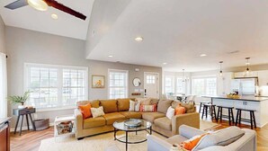 A spacious living area with a large sofa, a coffee table, and a kitchen in the background. - Town of Bethany Beach designer cottage with water views, alfresco porch & AC (Bethany Beach)