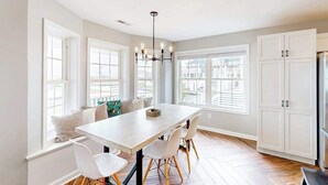 A modern kitchen with a central island, white cabinetry, and large windows. - Town of Bethany Beach designer cottage with water views, alfresco porch & AC (Bethany Beach)