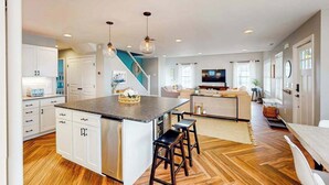 A modern kitchen with a central island, bar stools, and a staircase leading to another level. - Town of Bethany Beach designer cottage with water views, alfresco porch & AC (Bethany Beach)