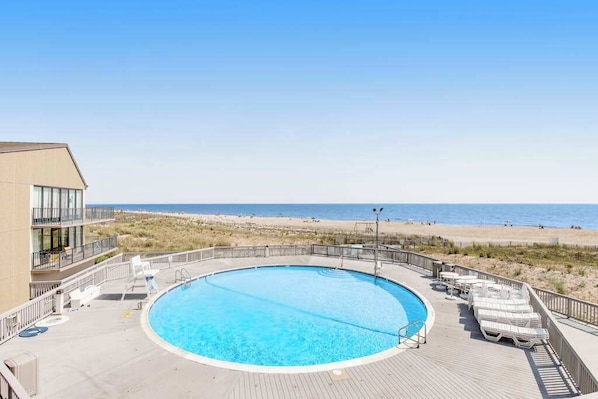 A pool with a view of the beach and ocean, surrounded by lounge chairs and a deck. - Experience fun at Sea Colony Bethany Beach - beach, tennis, & pickleball (Bethany Beach)