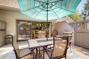An outdoor patio with a table and chairs, a large umbrella, and a view of the house interior through glass doors. - Experience fun at Sea Colony Bethany Beach - beach, tennis, & pickleball (Bethany Beach)
