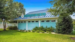 A building with a sign reading 'MILLVILLE BY THE SEA,' featuring a blue exterior and a white fence in the background. - Newly remodeled - dog friendly townhome with pools, tennis, washer/dryer & AC (Millville)