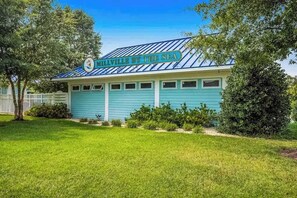 A building with a sign reading 'MILLVILLE BY THE SEA,' featuring a blue exterior and a white fence in the background. - Newly remodeled - dog friendly townhome with pools, tennis, washer/dryer & AC (Millville)