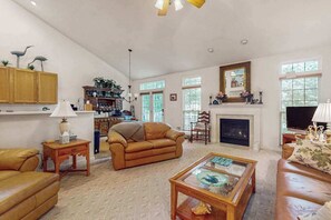 A living room with a fireplace, leather sofas, a coffee table, and a bookshelf. - South Hampton home with shared pool, game room, & water view- dog-friendly (Ocean View)