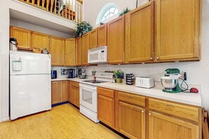 A kitchen with wooden cabinets, a white refrigerator, a microwave, a stove, and a mixer. - South Hampton home with shared pool, game room, & water view- dog-friendly (Ocean View)