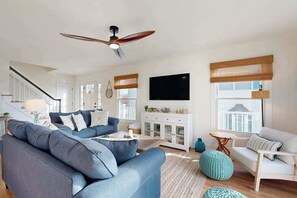 Ein modernes Wohnzimmer mit einem blauen Sofa, einem weißen Sessel, einem Holzschrank und einem Deckenventilator.