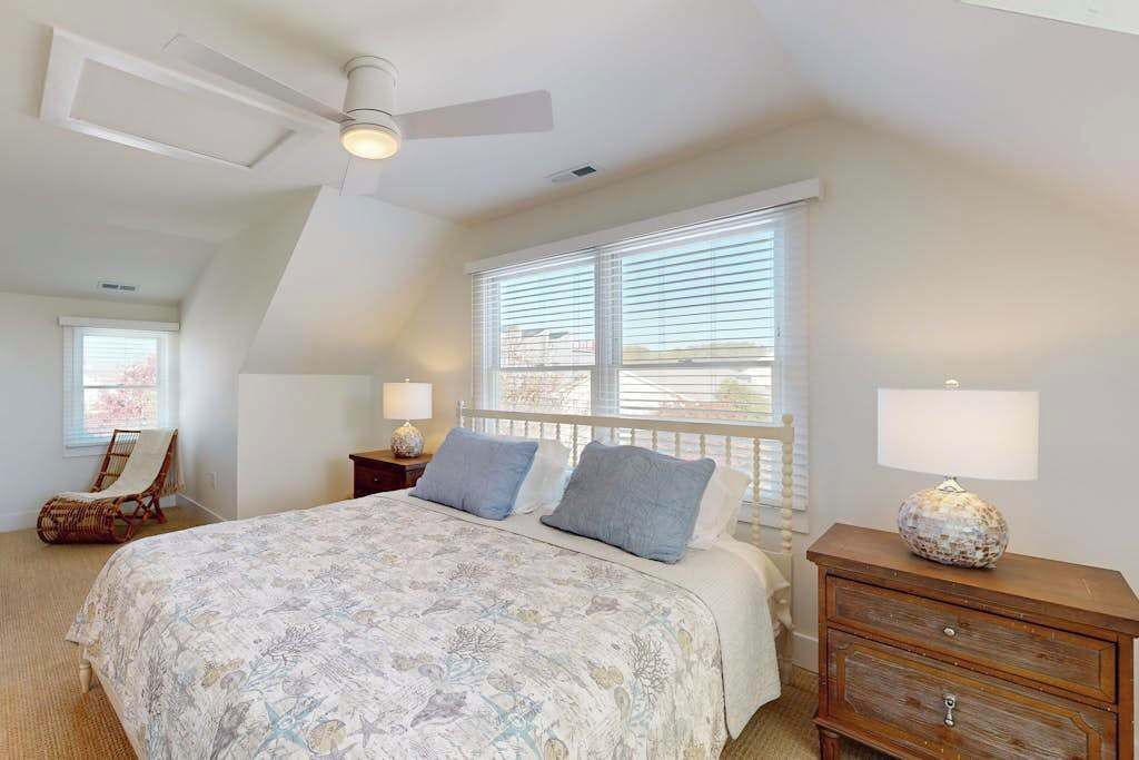 Ein Schlafzimmer mit Bett, Nachttisch, Kommode, Stuhl und Deckenventilator.