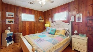 Una camera da letto con pareti in legno, un letto con copriletto, una ventola a soffitto e due finestre con persiane.