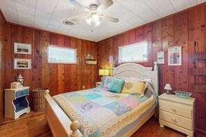 A bedroom with wooden walls, a bed with a quilt, a ceiling fan, and two windows with blinds. - Town of South Bethany waterfront home with boat ramp - 5-min walk to beach (Bethany Beach)