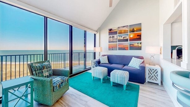 Un balcón con vista a la playa, un sofá azul, una silla de mimbre y una mesita.