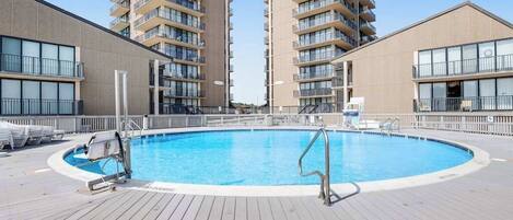 Une piscine entourée d’une terrasse en bois, avec deux immeubles de grande hauteur en arrière-plan.