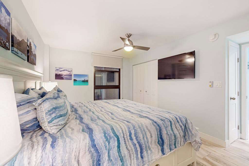 Een slaapkamer met een bed, een plafondventilator, een televisie en een deur.