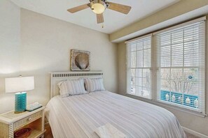 A bedroom with a bed, a ceiling fan, a window with blinds, and a wall-mounted artwork. - Bear Trap Dunes first floor condo w/community pool, tennis court & on site golf (Ocean View)