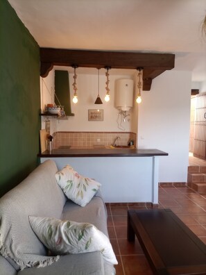 A cozy living area with a sofa, a bench, and a kitchen area with a sink and hanging lights. - Villa test Promotions (Roma)
