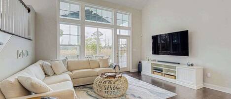 A spacious living room with a large window, a sofa, a coffee table, and a TV mounted on the wall.