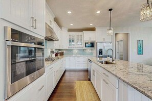 A modern kitchen with white cabinetry, stainless steel appliances, a granite countertop, and a central island. - Marlin Chase home with resort amenities, deck, grill, Free WIFI (Ocean View)