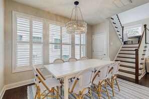A dining area with a white table and wicker chairs, a chandelier, and a staircase. - Marlin Chase home with resort amenities, deck, grill, Free WIFI (Ocean View)