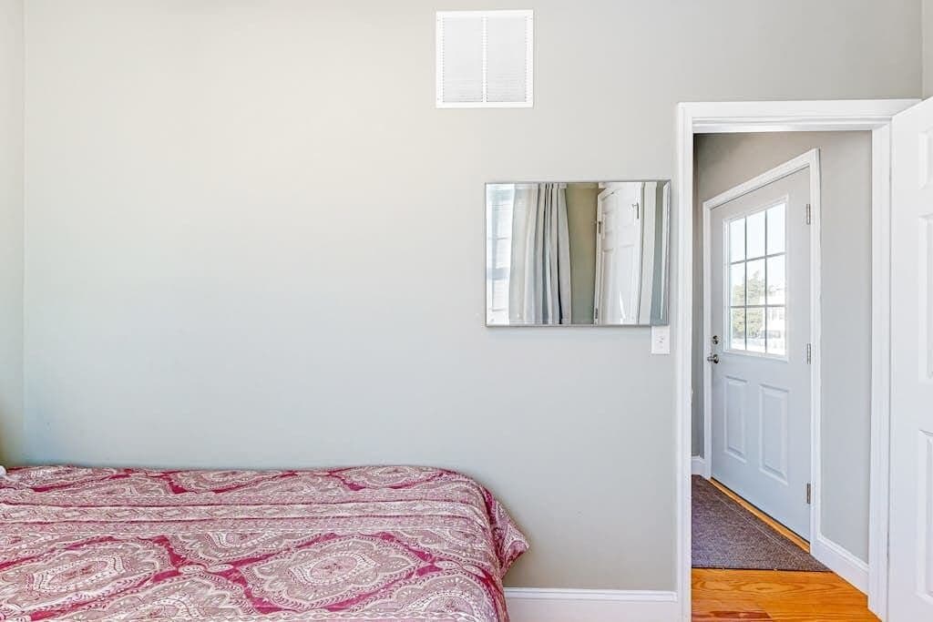 A bedroom with a patterned bedspread, a mirror on the wall, and a door leading to another room.