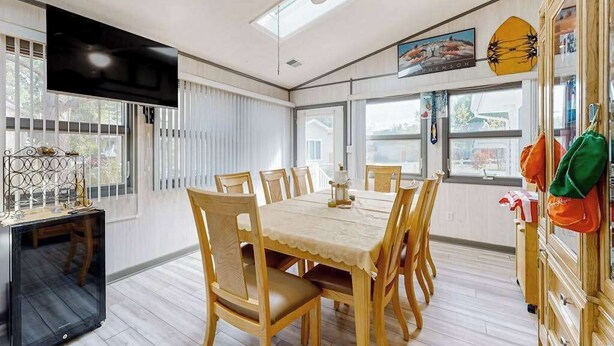 Un coin repas comprenant une table et des chaises, un ventilateur de plafond, un téléviseur et une fenêtre avec des stores.