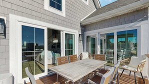 A deck with a wooden table and chairs, large sliding glass doors, and a view of the backyard. - Spacious pet friendly waterfront house w/deck, patio, balcony & gas grill (Bethany Beach)