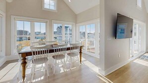 A spacious dining area with a large table and chairs, large windows, a ceiling fan, and a mounted TV. - Spacious pet friendly waterfront house w/deck, patio, balcony & gas grill (Bethany Beach)