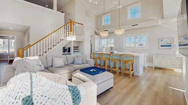 A spacious living area with a staircase, a dining area with bar stools, and a kitchen in the background. - Spacious pet friendly waterfront house w/deck, patio, balcony & gas grill (Bethany Beach)