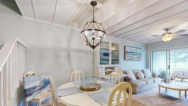 A dining area with a round table, chairs, and a chandelier. There is a sofa and a coffee table in the background. - Mallard Lakes townhouse in peaceful community with pool, hot tub, fishing pier (Selbyville)