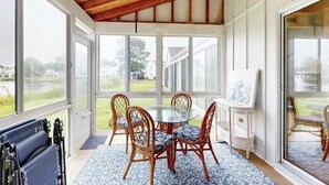 A conservatory with a glass table surrounded by wicker chairs, large windows, and a wooden ceiling. - Mallard Lakes townhouse in peaceful community with pool, hot tub, fishing pier (Selbyville)