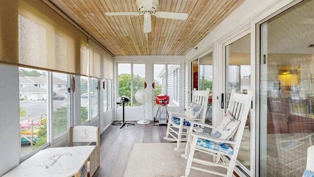A covered porch with a ceiling fan, rocking chairs, a table, and large windows. - Bay view condo with screened porch, pickleball, on-site golf and shared pool (Ocean View)