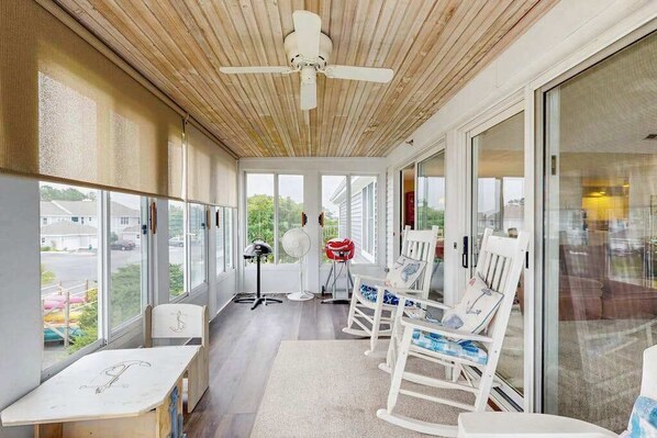 A covered porch with a ceiling fan, rocking chairs, a table, and large windows. - Bay view condo with screened porch, pickleball, on-site golf and shared pool (Ocean View)