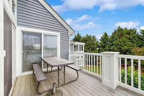 A covered deck with a picnic table and a sliding glass door. - Bay view condo with screened porch, pickleball, on-site golf and shared pool (Ocean View)