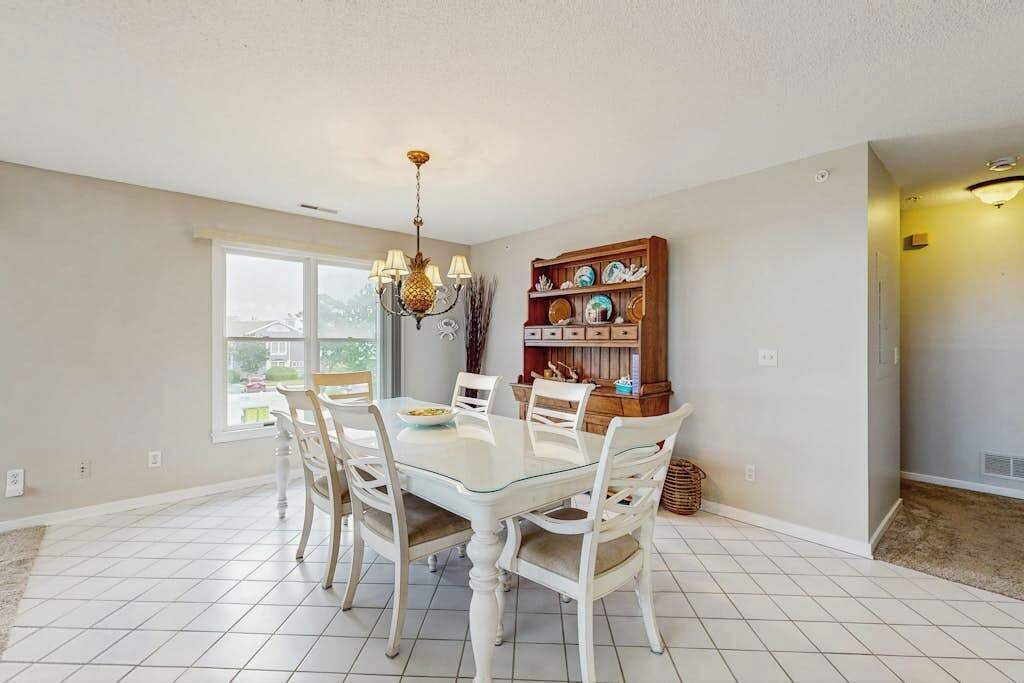 A dining area with a glass table, white chairs, a chandelier, and a bookshelf.