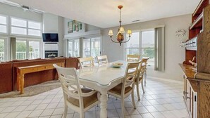 A spacious kitchen with a dining table, chairs, a chandelier, and a television. - Bay view condo with screened porch, pickleball, on-site golf and shared pool (Ocean View)