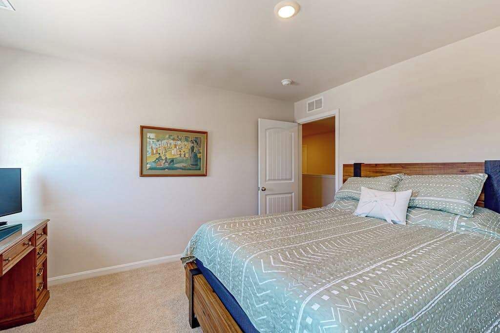 Une chambre à coucher avec un lit, un téléviseur posé sur une commode en bois, et une porte donnant sur une autre pièce.