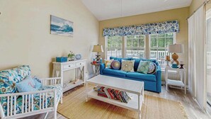 Un salon avec une table basse blanche, un canapé bleu, un fauteuil blanc et un ventilateur de plafond.