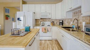 Une cuisine avec des meubles blancs, un plan de travail en granit, une cuisinière, un four à micro-ondes et un évier.