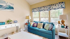 Un salon avec un canapé de couleur turquoise, une table basse blanche et un tableau représentant une vague accroché au mur.