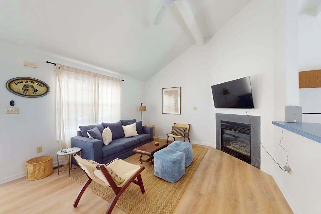 Una sala de estar con un sofá, otomanas, chimenea, televisor y un cuadro en la pared.