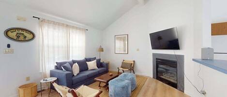Una sala de estar con un sofá, otomanas, chimenea, televisor y un cuadro en la pared.